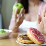 A woman rejects sugary treats like donuts for healthier alternatives like fruit and vegetables.